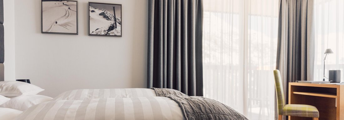 A modern bedroom with a cozy bed and elegant curtains. The room features a desk and some artwork on the wall. - 4 * Superior Hotel Schöne Aussicht - Hochsölden