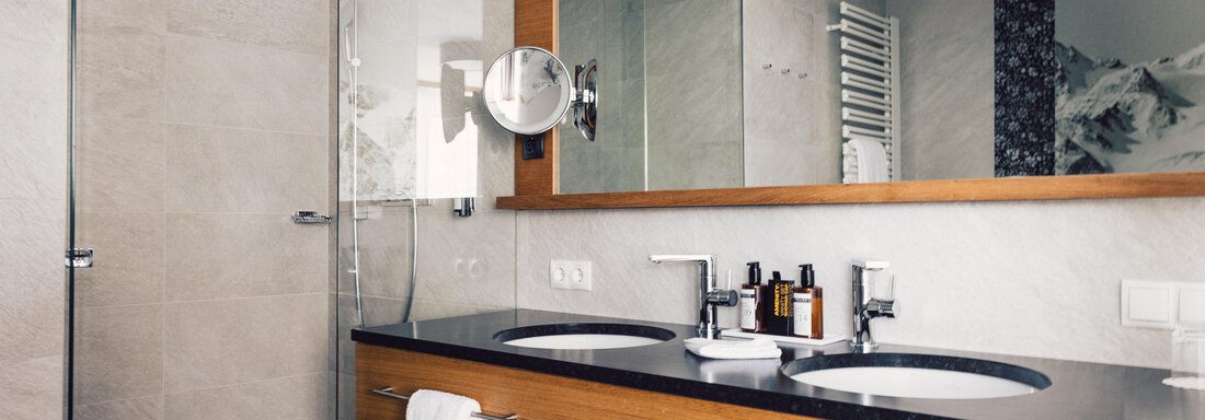 A modern bathroom with a shower and two sinks. The wooden paneling and large mirrors create a stylish atmosphere. - 4 * Superior Hotel Schöne Aussicht - Hochsölden
