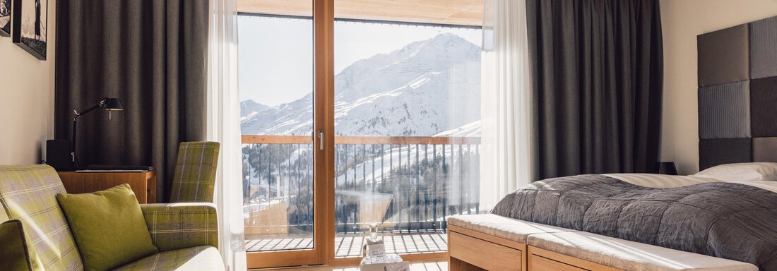 schoene_aussicht_w22_danielzangerl _508 A modern hotel room with a bed and a comfortable sofa. The room offers a view of the mountains through large windows. - 4 * Superior Hotel Schöne Aussicht - Hochsölden