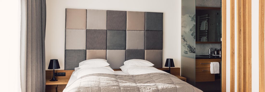 A modern bedroom with a double bed and a padded headboard. The walls are bright, and there is stylish furniture as well as soft light sources. - 4 * Superior Hotel Schöne Aussicht - Hochsölden