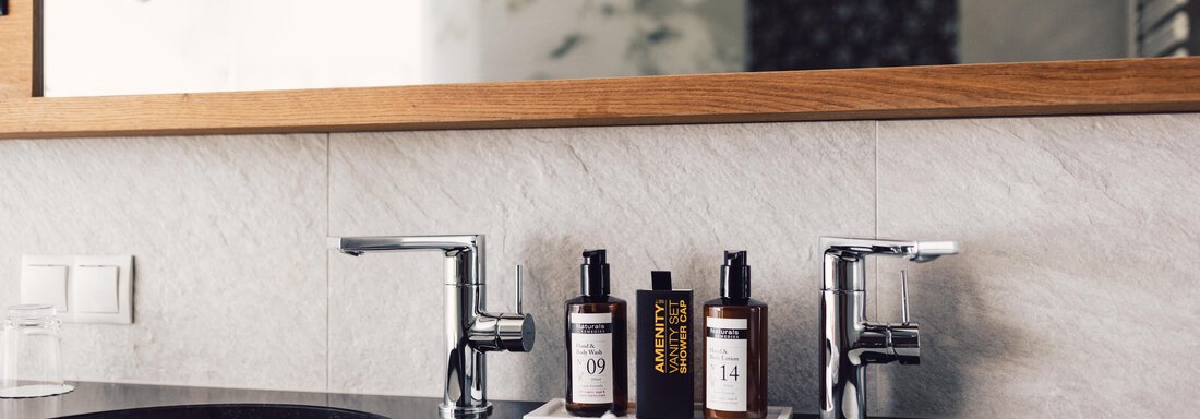A modern bathroom with two sinks and elegant faucets. High-quality toiletries and a towel are placed on the countertop. - 4 * Superior Hotel Schöne Aussicht - Hochsölden