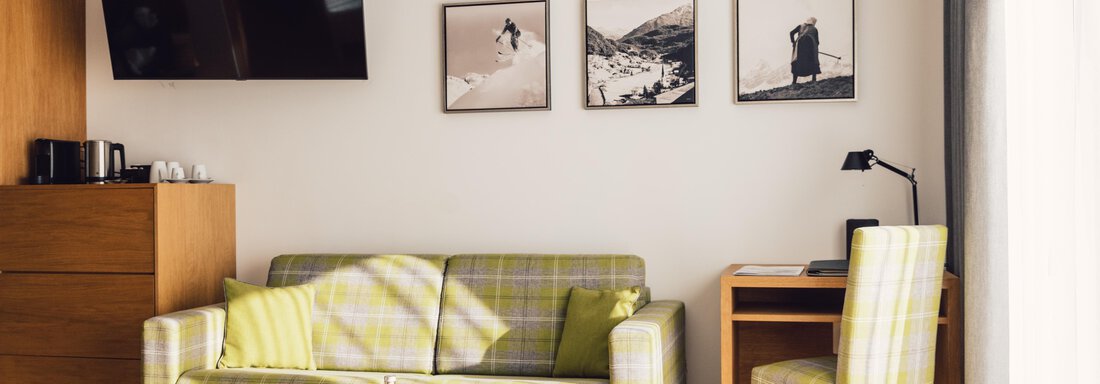A cozy hotel room with a sofa and a table. Pictures and a television are mounted on the wall. - 4 * Superior Hotel Schöne Aussicht - Hochsölden