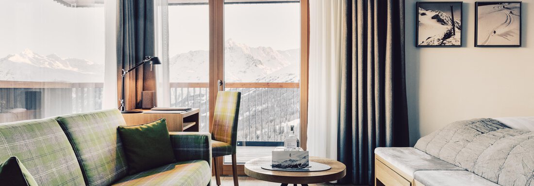 A modern living room with a cozy sofa and an armchair. Large windows provide a view of the mountains and let in a lot of light. - 4 * Superior Hotel Schöne Aussicht - Hochsölden