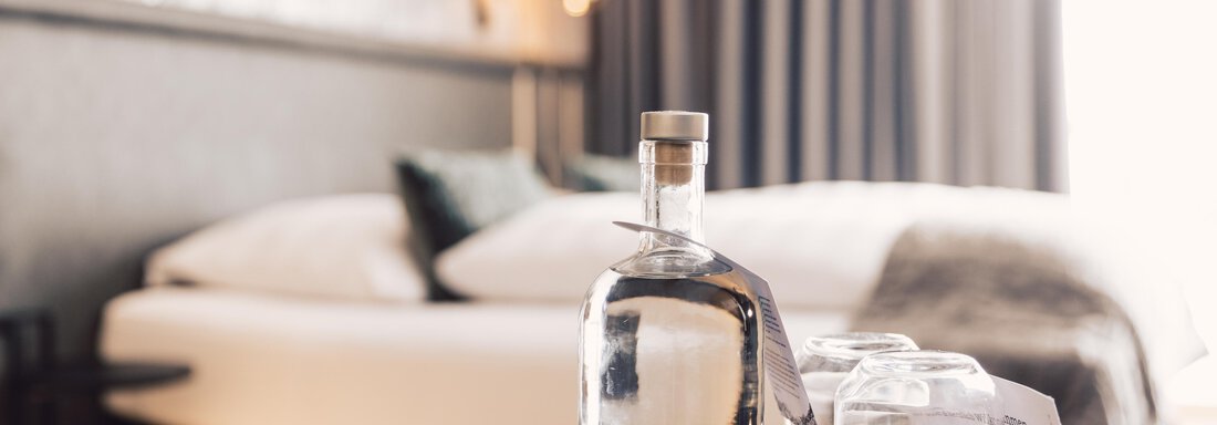 schoene_aussicht_w22_danielzangerl _686 An elegant hotel room with a modern bed and soft colors. On a table, there is a glass bottle of water and two glasses. - 4 * Superior Hotel Schöne Aussicht - Hochsölden