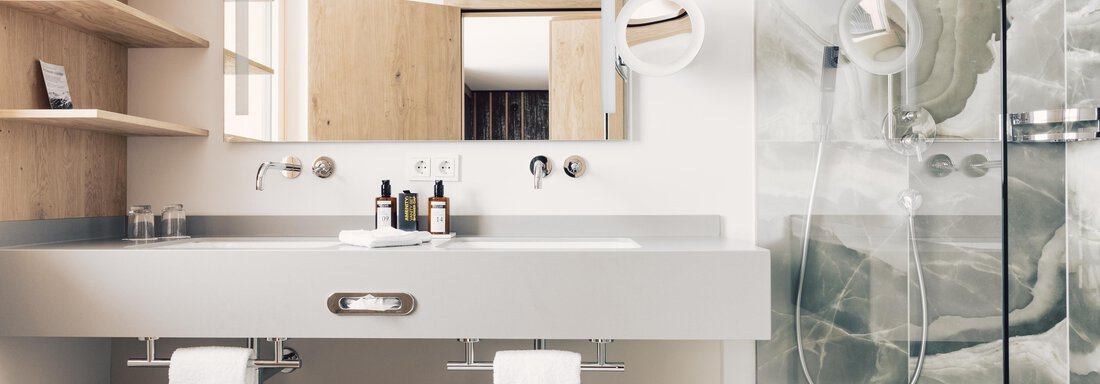 A modern bathroom with an elegant sink and a large mirror. The shower is separated by a glass door and features a stylish tile design. - 4 * Superior Hotel Schöne Aussicht - Hochsölden