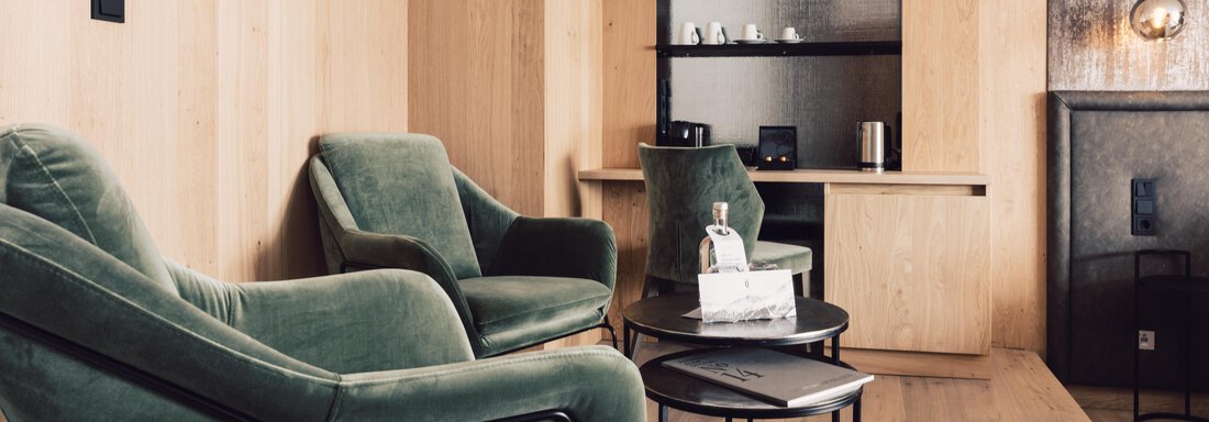 An elegant room with two green armchairs and a small table. The walls are made of light wood, and there are shelves in the background. - 4 * Superior Hotel Schöne Aussicht - Hochsölden