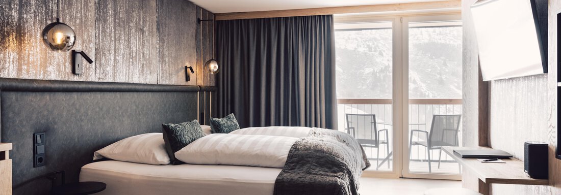 A modern hotel room with a double bed, cozy furnishings, and large windows. The room offers a view of a balcony and is designed in neutral colors. - 4 * Superior Hotel Schöne Aussicht - Hochsölden