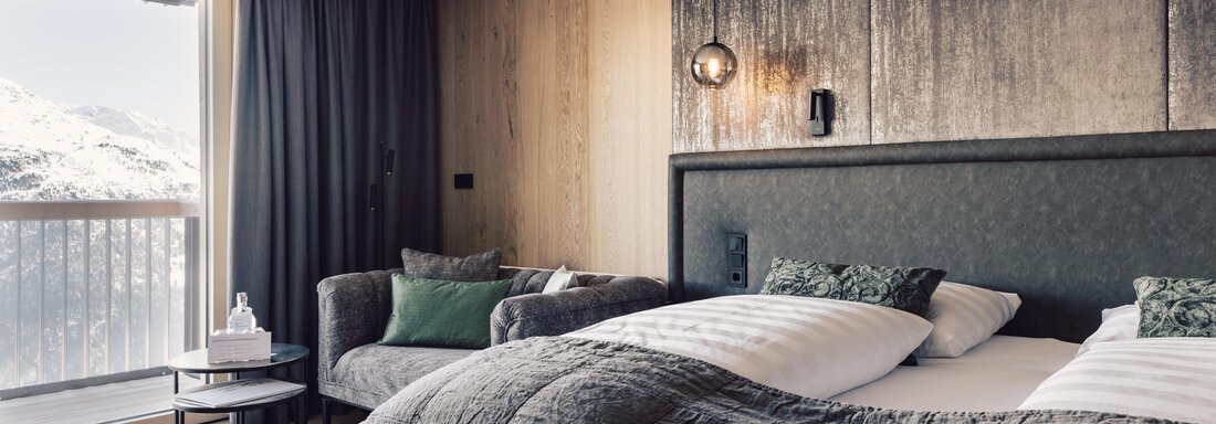 A modern hotel room with two beds and a cozy sofa. Large windows offer a view of the mountains. - 4 * Superior Hotel Schöne Aussicht - Hochsölden