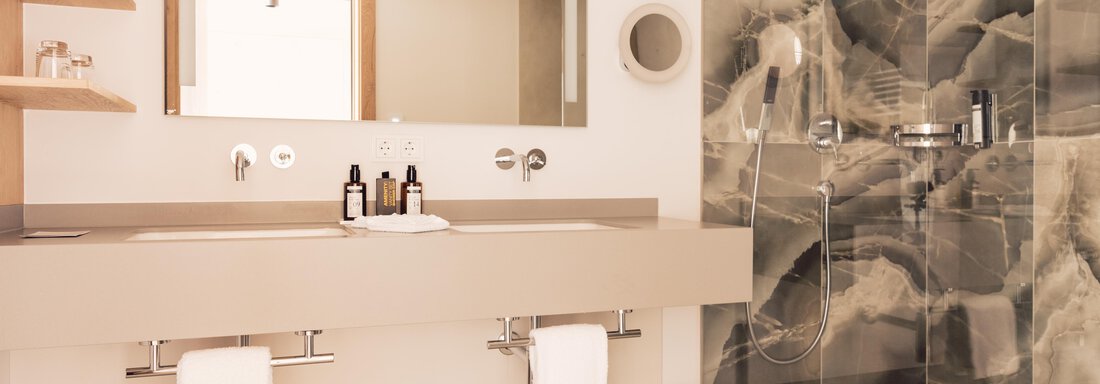 A modern bathroom with an elegant sink and large mirror. The shower wall has an appealing, marbled design. - 4 * Superior Hotel Schöne Aussicht - Hochsölden