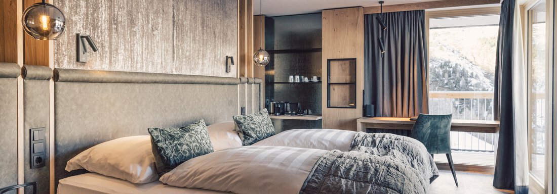A modern hotel room with two single beds and elegant decor. Large windows provide plenty of natural light and a view outside. - 4 * Superior Hotel Schöne Aussicht - Hochsölden