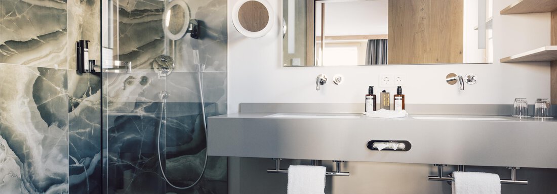 A modern bathroom with a stylish shower cubicle and an elegant sink. The wall features an appealing design in gray and green tones. - 4 * Superior Hotel Schöne Aussicht - Hochsölden