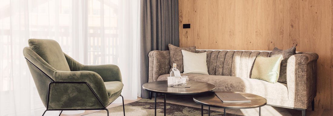 A stylish living room with a cozy sofa and an armchair. A round table sits on an elegant rug, and large windows provide plenty of daylight. - 4 * Superior Hotel Schöne Aussicht - Hochsölden