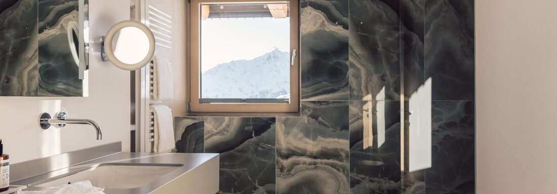 A modern bathroom with elegant black marble accents. The window offers a view of the mountains and provides natural light. - 4 * Superior Hotel Schöne Aussicht - Hochsölden