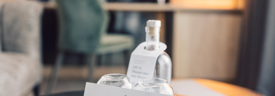 A stylish table with a glass bottle and two glasses. In the background, a bright room with a chair can be seen. - 4 * Superior Hotel Schöne Aussicht - Hochsölden