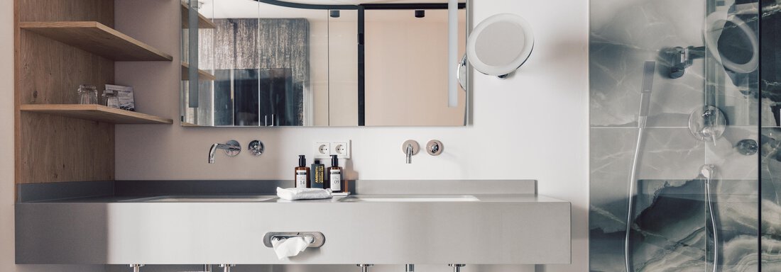 A modern bathroom with a large mirror and an elegant sink. The walls are painted in soft colors, and a shower is also available. - 4 * Superior Hotel Schöne Aussicht - Hochsölden