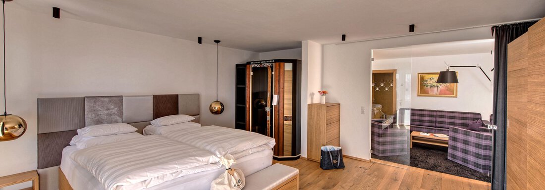 Bedroom A modern bedroom with a double bed and wooden flooring. In the background, there is a cozy living area and a wardrobe. - 4 * Superior Hotel Schöne Aussicht - Hochsölden