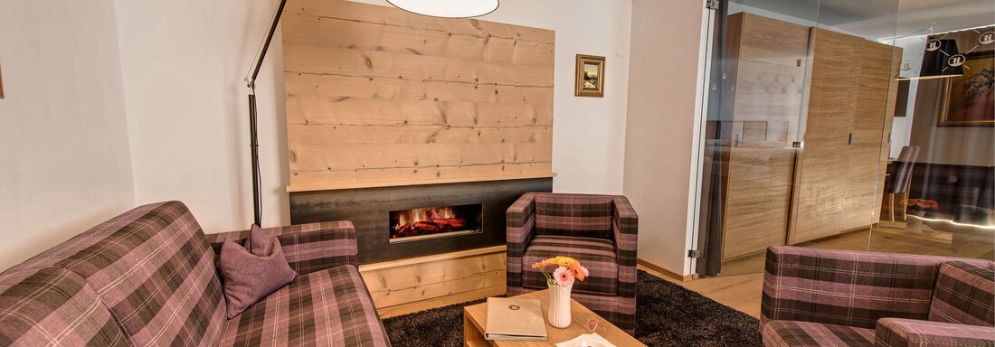 A cozy living room with plaid sofas and a modern fireplace. The room is bright and inviting, with a wooden shelf and a small table in the center. - 4 * Superior Hotel Schöne Aussicht - Hochsölden
