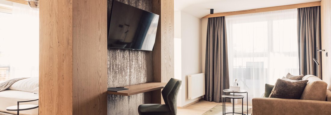 schoene_aussicht_w22_danielzangerl _360 A modern room with wood and fabric elements. There is a TV, a desk, and a comfortable sofa, as well as large windows for plenty of daylight. - 4 * Superior Hotel Schöne Aussicht - Hochsölden
