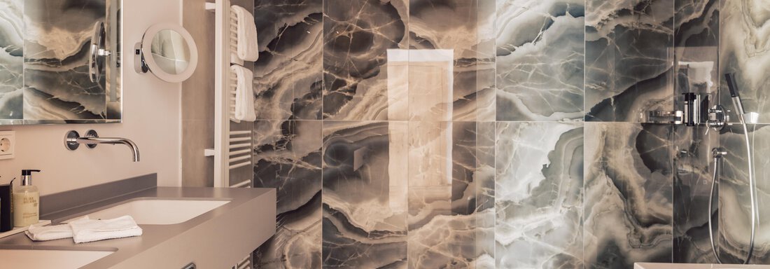 A modern bathroom with elegant design and large, marbled tiles. There is a shower, a sink, and a bathtub that convey a luxurious impression. - 4 * Superior Hotel Schöne Aussicht - Hochsölden