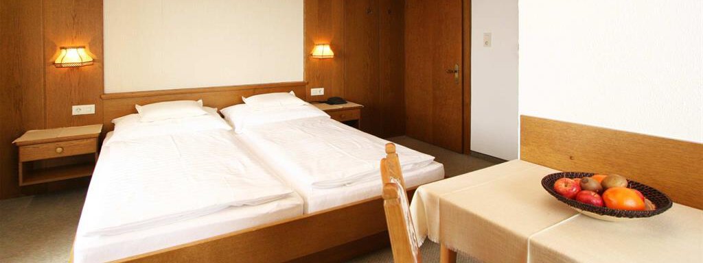 Doppelzimmer A cozy hotel room with two single beds and warm wood interiors. On the table to the right, there is a bowl of fruit. - Pension Ferdinand - Hochsölden