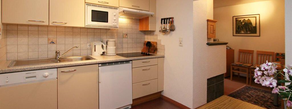 Küche A modern kitchen with bright cabinets and a countertop. There is a fruit bowl with various fruits on the table. - Pension Ferdinand - Hochsölden