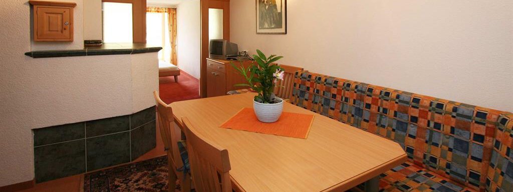A cozy dining area with a wooden table and a colorful seating corner. A plant is placed in the middle of the table, creating a friendly atmosphere. - Pension Ferdinand - Hochsölden