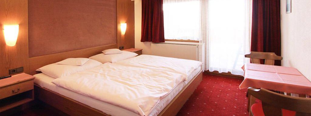 A cozy hotel room with a double bed and red carpet. Large windows let in plenty of daylight. - Pension Ferdinand - Hochsölden