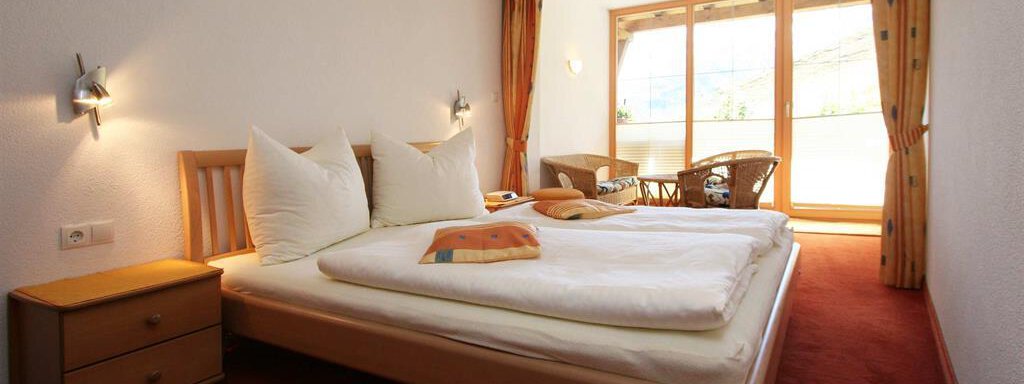 A cozy bedroom with a double bed and wooden details. Large windows let in plenty of light and offer a view outside. - Pension Ferdinand - Hochsölden