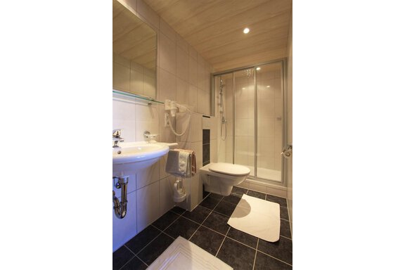 A modern bathroom with a shower, a sink, and a toilet. The floor is tiled in black and the walls are tiled in light colors. - Pension Ferdinand - Hochsölden