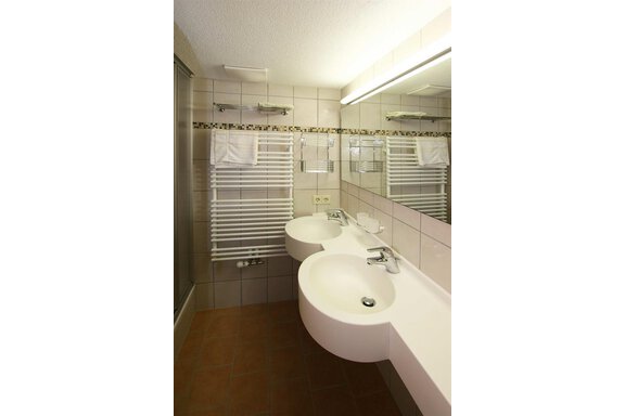 A modern bathroom with two sinks and a large mirror. The walls are brightly tiled and there is a towel radiator. - Pension Ferdinand - Hochsölden
