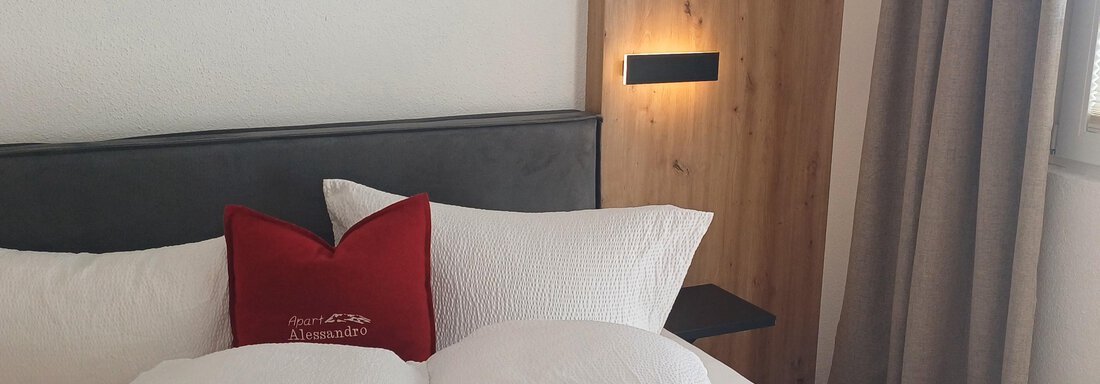 Ein gemütliches Schlafzimmer mit einem großen Bett und weichen Kissen. Die Wände sind hell und es gibt ein Fenster mit Vorhängen. - Apart Alessandro - Huben