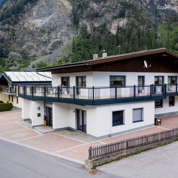 Ein modernes Haus mit einem Balkon in einer malerischen Umgebung. Die Landschaft wird von Bergen und Bäumen umgeben. - Appart Sporthütte Fiegl Huben - Huben