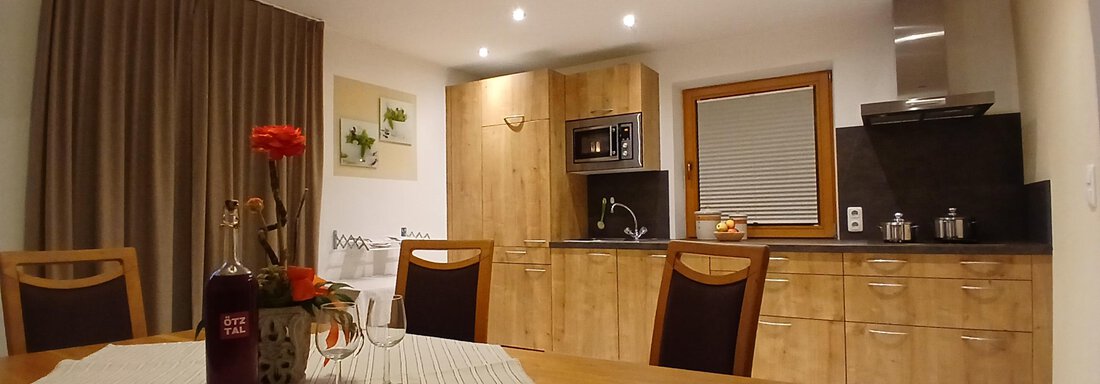Eine moderne Küche mit Holzschränken und hellem Licht. Der Essbereich hat einen Holztisch und hübsche Blumendeko. - Appartement Erich Wilhelm - Huben