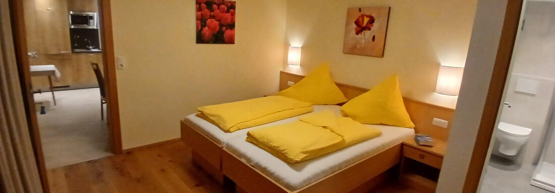 Ein gemütliches Schlafzimmer mit einem Doppelbett und gelben Kissen. Der Raum hat helle Wände und modernes Mobiliar aus Holz. - Appartement Erich Wilhelm - Huben