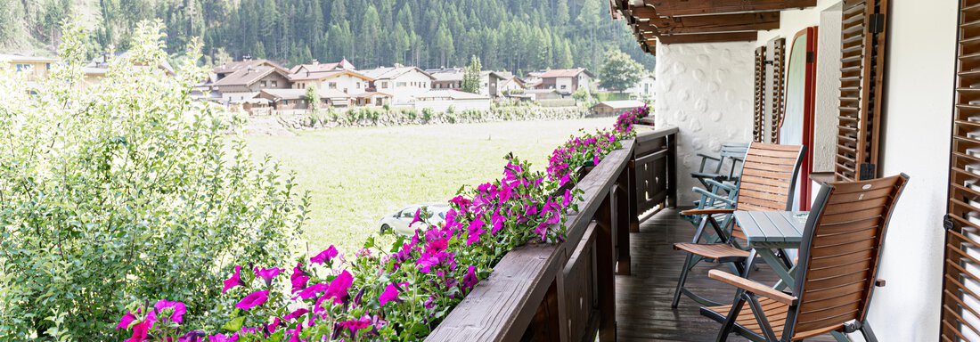 Ein Balkon mit bunten Blumen und Stühlen, umgeben von einer grünen Berglandschaft. Die Atmosphäre ist ruhig und einladend. - Appartements Alpenrose - Huben