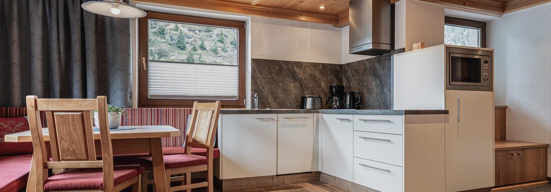 Eine moderne Küche mit einem Essbereich aus Holz und roten Polstern. Große Fenster sorgen für viel Tageslicht und Ausblick auf die Natur. - Appartements Alpenrose - Huben