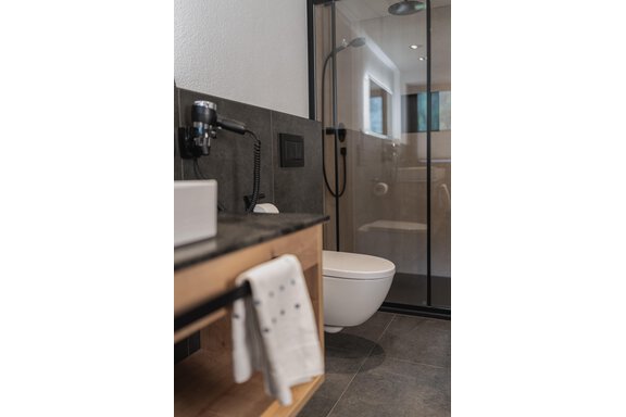 Ein modernes Badezimmer mit einer Dusche und einer Toilette. Es hat elegante Fliesen und Holzdetails. - Appartements Alpenrose - Huben
