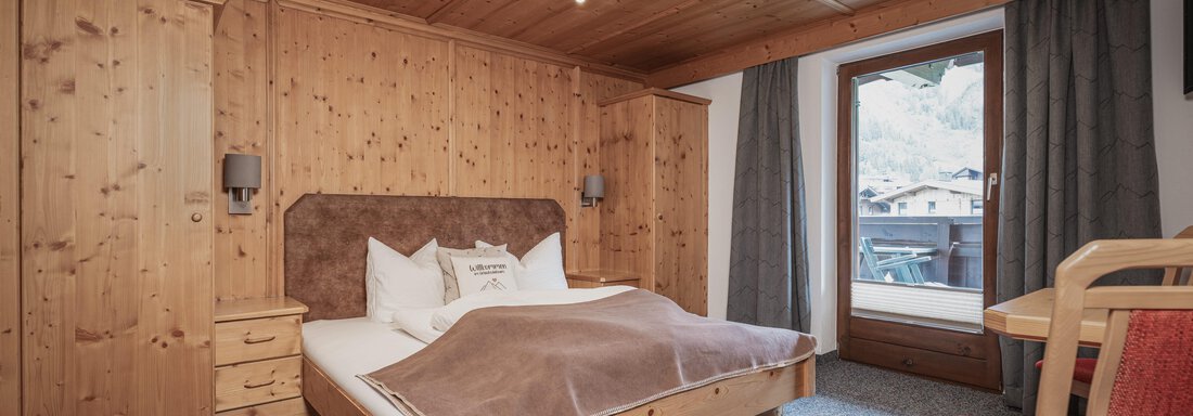 Ein gemütliches Zimmer mit Holzvertäfelung und einem großen Bett. Der Raum verfügt über einen Balkon mit Blick auf die Berge. - Appartements Alpenrose - Huben
