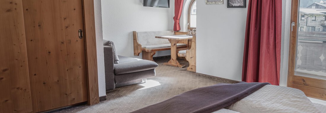 Ein gemütliches Schlafzimmer mit einem großen Bett und Holzdetails. Der Raum verfügt über einen Essbereich und Zugang zu einem Balkon mit Blick nach draußen. - Appartements Alpenrose - Huben