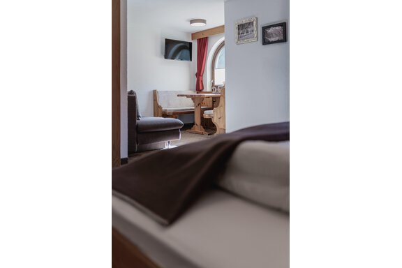 Ein gemütlicher Innenraum mit einem Sofa, einem Tisch und einem Fernseher. Die Fenster sind mit roten Vorhängen dekoriert und viel Licht fällt in den Raum. - Appartements Alpenrose - Huben
