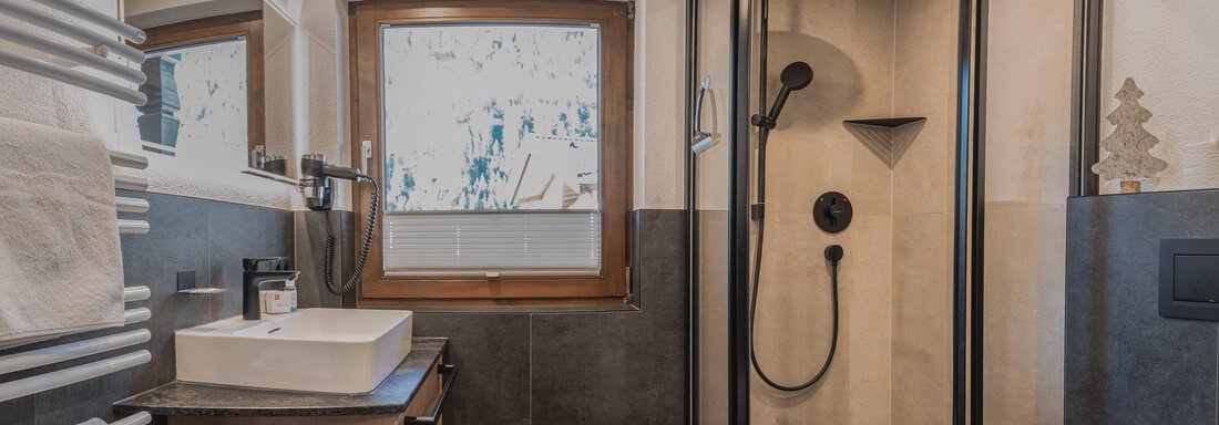 Ein modernes Badezimmer mit einer Dusche und einer großen Fensterfläche. Der Holzboden und die stilvolle Einrichtung sorgen für eine gemütliche Atmosphäre. - Appartements Alpenrose - Huben