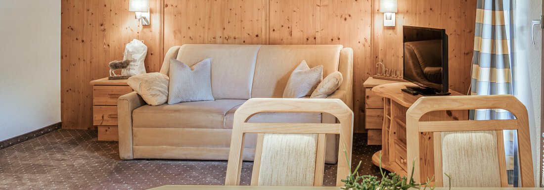 Ein gemütliches Wohnzimmer mit Holzverkleidung. Eine bequeme Couch, ein Tisch und dekorative Elemente schaffen eine einladende Atmosphäre. - Appartements Alpenrose - Huben