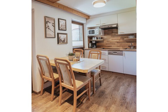Eine moderne Küche mit einem Esstisch und vier Stühlen. An der Wand hängen Bilder, und die Einrichtung hat warme Holzdetails. - Appartements Alpenrose - Huben