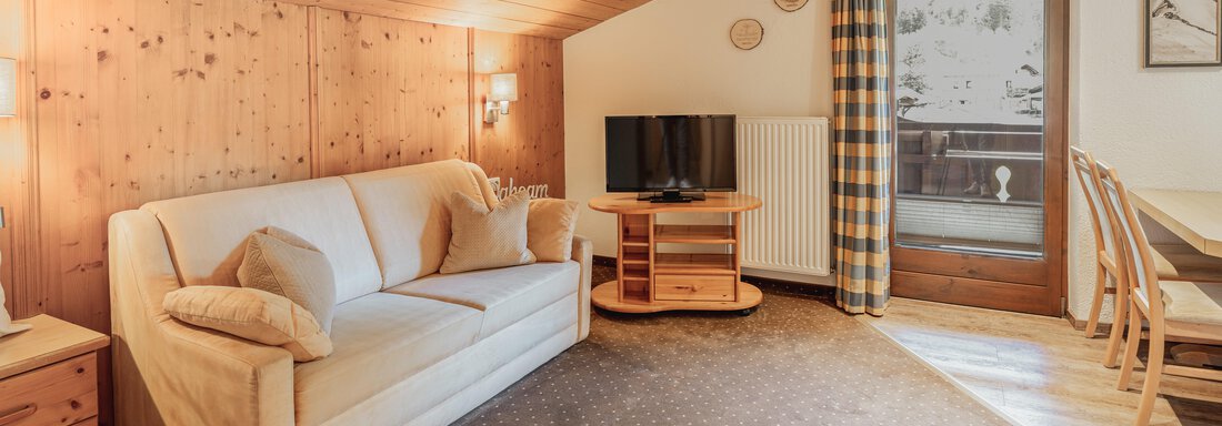 Ein gemütlicher Wohnbereich mit einem hellen Sofa und einem Tisch. Große Fenster bieten einen Blick nach draußen und Holzverkleidung schafft eine einladende Atmosphäre. - Appartements Alpenrose - Huben