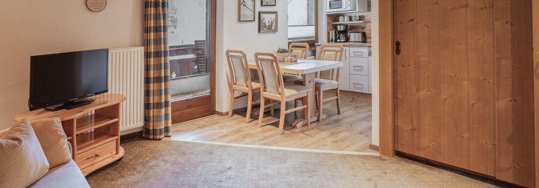 Ein gemütlicher Wohnraum mit einer Essecke und einer modernen Küchenzeile. Das Zimmer hat helle Holzelemente und große Fenster, die viel Licht hereinlassen. - Appartements Alpenrose - Huben
