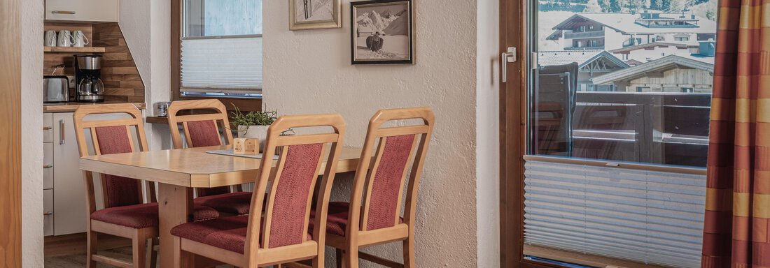 Ein gemütlicher Essbereich mit einem Holztisch und Stühlen in warmen Farben. Durch das Fenster ist eine schöne Aussicht auf die Berge zu sehen. - Appartements Alpenrose - Huben