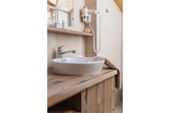 Ein modernes Badezimmer mit einem runden Waschbecken auf einem Holzregal. Im Hintergrund sind ein Spiegel und ein Fön sichtbar. - Appartements Alpenrose - Huben