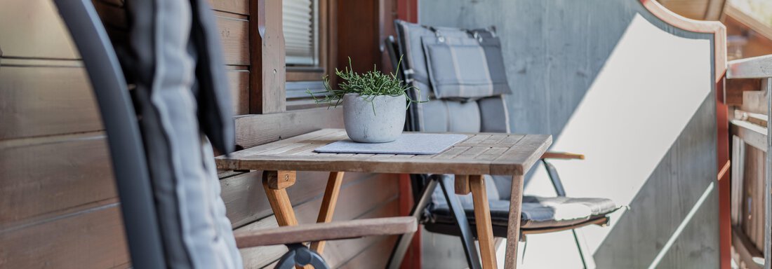 Ein gemütlicher Balkon mit Holzmöbeln und einem kleinen Tisch. Auf dem Tisch steht ein Blumentopf mit Pflanzen. - Appartements Alpenrose - Huben