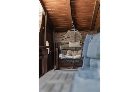 Ein gemütlicher Hängestuhl mit Kissen hängt in einem Holzhaus. Die Umgebung ist warm und einladend. - Appartements Alpenrose - Huben