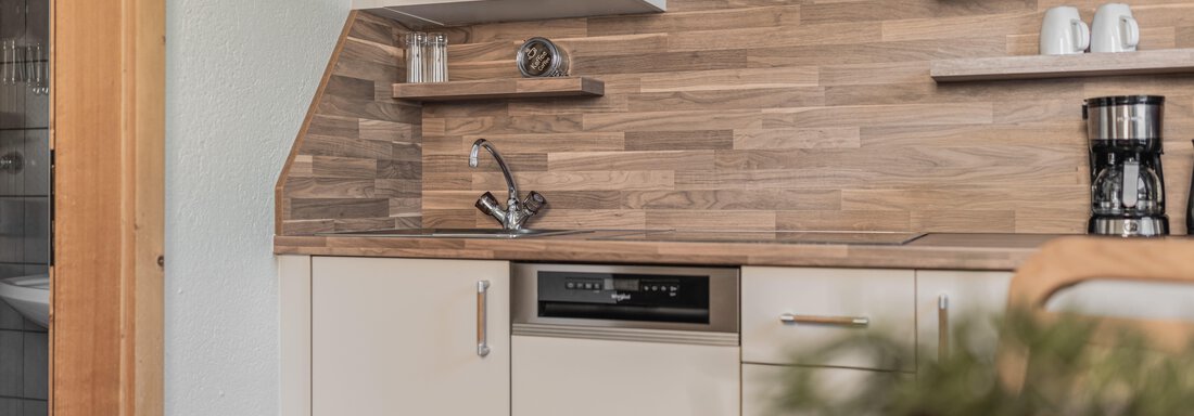 Eine moderne Küche mit Holzverkleidung und integrierten Geräten. Sie zeigt einen Mikrowellenofen, eine Spüle und eine Kaffeemaschine. - Appartements Alpenrose - Huben